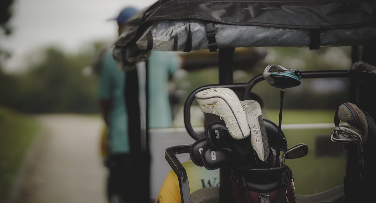 Close-up of golf clubs in a cart on a lush green course, ready for a day of golfing.